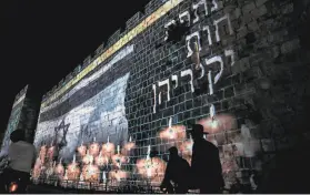  ?? Ahmad Gharabli / AFP via Getty Images ?? An image of the Israeli flag and candles appears Sunday on a wall of Jerusalem’s Old City during a day of mourning for the stampede victims.