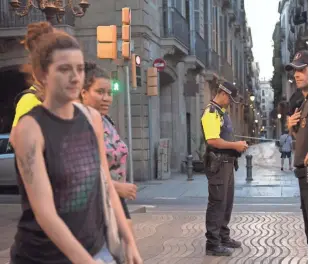  ?? CARL COURT, GETTY IMAGES ?? Women walk past police officers patrolling on Las Ramblas on Friday following Thursday’s terrorist attack in Barcelona.