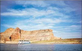  ?? Antelope Point Marina ?? A HOUSEBOAT floats on Lake Powell near a giant rock outcrop on the shore.