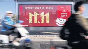  ?? REUTERS ?? People pass by a JD.com advert for Singles Day shopping, in Beijing last October.