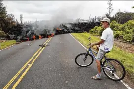  ?? MARCO GARCIA / ASSOCIATED PRESS ?? Leilani Estates resident Sam Knox watches lava stretch across the road Saturday in Pahoa, Hawaii. Knox’s home is less than a few hundred yards from the lava flow, but he does not have any plans to evacuate.