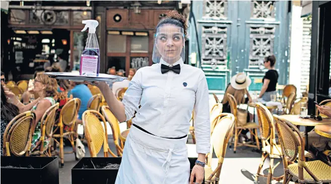  ??  ?? A waitress at La Palette, in Paris, uses protective equipment and hygiene spray while serving at outdoor tables, as bars and restaurant­s reopened yesterday after 10 weeks of lockdown