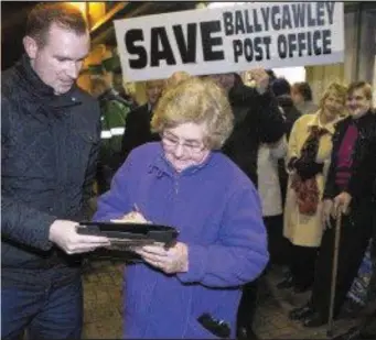  ??  ?? A woman signs a petition along with Thomas Walsh at a protest to save Ballygawle­y Post Office.