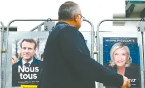  ?? AP PHOTO/BOB EDME ?? A man walks past presidenti­al campaign posters of French president Emmanuel Macron, a centrist candidate for re-election, and far-right presidenti­al candidate Marine Le Pen in Anglet, southweste­rn France on Wednesday.