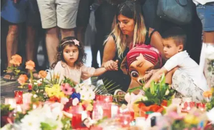  ?? Javier Soriano, AFP/Getty Images ?? A woman and two children look at flowers, candles and other items set up on Las Ramblas in Barcelona, Spain, on Friday as they pay tribute to the 13 people killed in Thursday’s attack in the city.