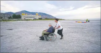  ??  ?? Robert Atkinson, 91, is pushed by daughter Laurie Conklin along the receding shoreline before his flight over the Great Salt Lake near Salt Lake City. When he returned this year to fly over the lake in a motorized paraglider, he found it changed. “It’s much shallower than I would have expected it to be,” he said.