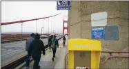  ??  ?? People walk past an emergency phone and numbers for crisis counseling on the Golden Gate Bridge