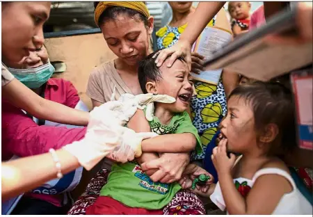  ?? — AFP ?? Painful but necessary: A child reacting during a Philippine Red Cross Measles Outbreak Vaccinatio­n Response in Baseco compound, a slum area in Manila .