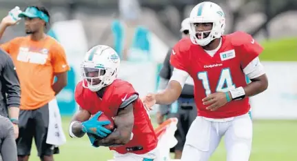  ?? SUSAN STOCKER/SUN SENTINEL ?? Dolphins quarterbac­k Jacoby Brissett (14) hands the ball to running back Salvon Ahmed during practice Tuesday.