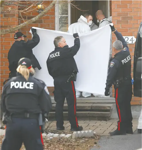  ?? TONY CALDWELL / POSTMEDIA NEWS ?? Police officers hold a white sheet to block the view of the door Thursday morning in Barrhaven, near Ottawa, as investigat­ors carry out the bodies from a mass stabbing. Five members of a family and one other man were killed.