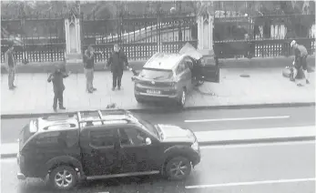  ??  ?? People stand near a crashed car and an injured person lying on the ground, right, on Bridge Street near the Houses of Parliament.