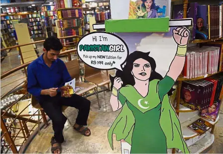  ?? — AFP ?? It’s a bird, it’s a plane, it’s ... : A customer reading a ‘Pakistan Girl’ comic near a life-sized cutout of the superhero at a book store in Islamabad. The comic series attempts to fill a shortage of female role models and superheroe­s in mainstream...
