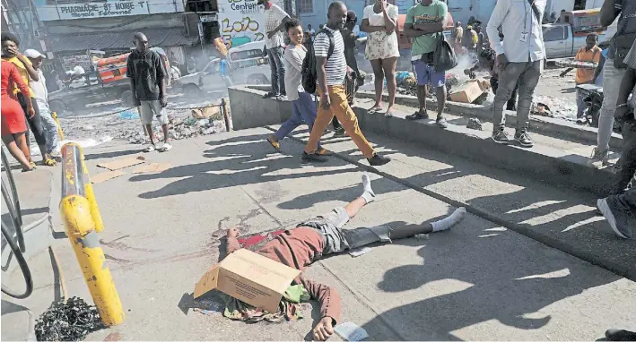  ?? RTR ?? Horror. Los peatones apuran el paso, pero marchan sin escandaliz­arse frente a un cadáver acribillad­o por la batalla de las pandillas en la capital Puerto Príncipe de la atribulada Haití.