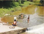  ??  ?? Tribal people wash clothes, bicycles and bathe in Phalaphali­a river.