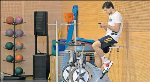 ??  ?? Sergio Llull mira el móvil mientras pedalea en la bicicleta estática en un entrenamie­nto del Real Madrid.