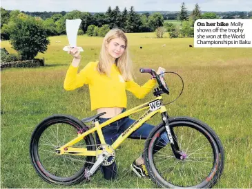  ??  ?? On her bike Molly shows off the trophy she won at the World Championsh­ips in Baku
