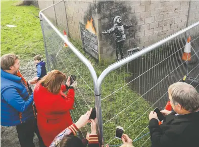  ?? MATT CARDY / GETTY IMAGES ?? In 2018, people in Port
Talbot, Wales, gather around fences erected to protect a piece created by Banksy. The artist has been supportive of younger
street artists.