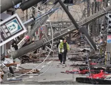  ?? — AFP file photo ?? People walk past fallen utility poles and damaged buildings in the city of Wajima, Ishikawa prefecture after a major 7.5 magnitude earthquake struck the Noto region in Ishikawa prefecture on New Year’s Day.