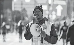  ?? JUNFU HAN/DETROIT FREE PRESS ?? Volunteer Deiontae Nicholas cheers marathon and half marathon runners and reminds them to follow their routes on Cass Avenue.