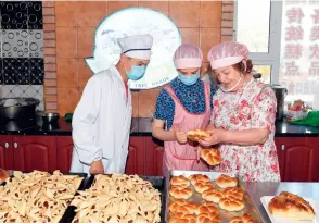  ??  ?? Dans une pâtisserie située dans le centre-ville de Tacheng, Zaitunna Kalimuwa explique au couple Yibadati Abulizi comment faire du pain.