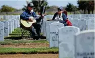  ??  ?? Gustavo Soltero, left, plays guitar as he and his wife, Maria Adela, visit the grave site of their son, Omar Soltero, on Wednesday. The Solteros’ son was killed in action in Afghanista­n in 2011 while serving as a specialist in the Army. The parents sang hymns and read passages from the Bible after laying a bouquet of flowers by their son’s headstone.