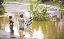  ?? AFPPIX ?? Residents watch as floodwater­s caused by Cyclone Debbie recede in Beenleigh yesterday.