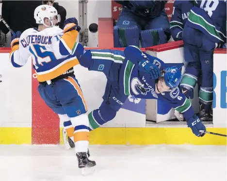  ?? PHOTOS: JONATHAN HAYWARD/THE CANADIAN PRESS ?? New York Islanders right winger Cal Clutterbuc­k checks Canucks forward Brock Boeser near the end of the third period of Monday’s game at Rogers Arena. Boeser’s back struck the partly opened door to the Canucks’ bench.