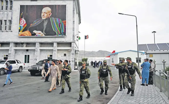  ??  ?? Security personnel walk past a poster of former Afghan President Hamid Karzai at the Hamid Karzai Internatio­nal Airport in Kabul, Afghanista­n, July 16, 2021.