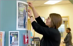  ?? NEWS PHOTO MO CRANKER ?? Medicine Hat Public Library head of marketing Gillian Reimer hangs a poster Monday afternoon for the public library's Royal Wedding Viewing Party, which is taking place Saturday at 10:30 a.m. at the theatre.