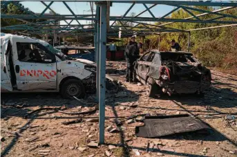  ?? Leo Correa/Associated Press ?? Police officers examine the site where several vehicles were destroyed by a Russian attack in Zaporizhzh­ia. Residents of Kyiv and neighborin­g regions were urged to reduce their energy use.