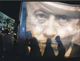  ?? Abir Sultan EPA/Shuttersto­ck ?? PROTESTERS on Saturday carry a banner showing Prime Minister Benjamin Netanyahu, whose law sparked a moral insurrecti­on among the Israeli public.