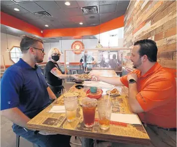  ?? RICARDO RAMIREZ BUXEDA/ORLANDO SENTINEL ?? Alex Wilkinson, left, and Michael Durant get food from Christina Bishop as they have lunch at Hawkers Asian Street Fare in Orlando.