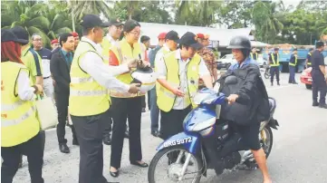  ??  ?? Dr Jerip (second right) gives advice to a motorcycli­st as Abang Mohd Porkan hands Davina an approved motorcycle helmet.