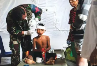  ?? AP PHOTO BY FAUZY CHANIAGO ?? A military paramedic tends to a boy who suffered a head injury from Sunday’s earthquake at a makeshift hospital in Kayangan, Lombok Island, Indonesia, on Wednesday.