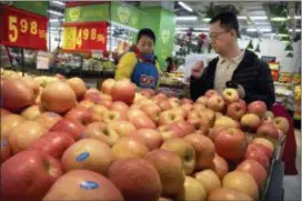  ?? MARK SCHIEFELBE­IN — THE ASSOCIATED PRESS ?? A woman wearing a uniform with the logo of an American produce company helps a customer shop for apples at a supermarke­t in Beijing, Friday. China announced a $3 billion list of U.S. goods including pork, apples and steel pipe on Friday that it said...