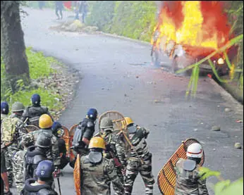  ?? AFP ?? Police personnel take cover near a burning car during clashes with Gorkha Janmukti Morcha supporters in Darjeeling on Thursday.