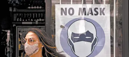  ?? JAE C. HONG/AP ?? A woman walks past a sign at a California liquor store telling customers they must have a mask on before entering.