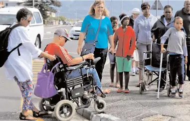  ?? PICTURE: CINDY WAXA ?? PITFALLS: Shireen Sachse helps wheelchair-bound Ashton Davids cross a road. A group of people in wheelchair­s from a retirement home in Muizenberg took part in a walk to highlight challenges facing the disabled.