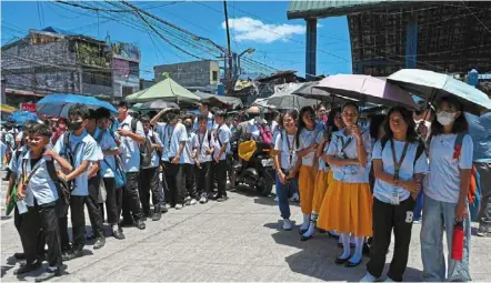  ?? — Photos: AFP ?? students use umbrellas to protect themselves from the sun as they line up to wait for their classes outside their school in Manila.