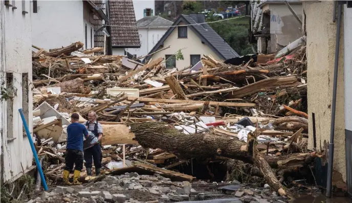  ?? GETTY IMAGES, ABOVE; AP, BELOW ?? TRAGEDY: Two men try to recover items Thursday next to a pile of debris left after flooding in Schuld, Germany, destroyed homes and left a trail of death in its wake. Below, people are rescued aboard rubber rafts in Liege, Belgium, after the Meuse River burst its banks.