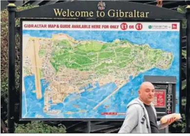  ??  ?? Un hombre pasa con el almuerzo por delante de un mapa turístico del Peñón.