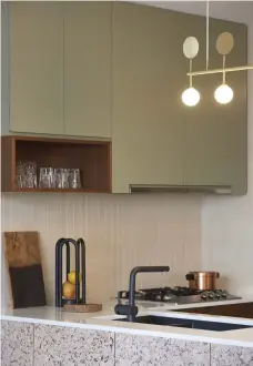  ??  ?? Above
Tan incorporat­ed splashes of classic mid-century colours throughout, seen here in the sage cabinets and cork-panelled counter in the kitchen. A brushed-brass Atelier Areti pendant lamp continues the theme and enlivens the space