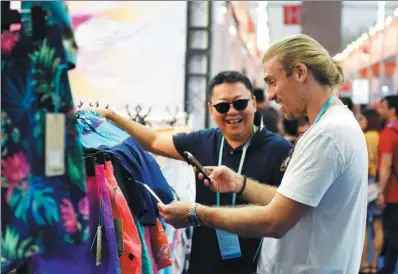  ?? XINHUA ?? A merchant examines clothes on sale at the Guangzhou Import and Export Fair in May.
