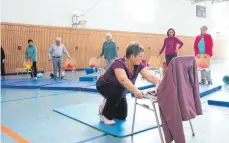  ??  ?? Mithilfe eines Stuhls zeigt Übungsleit­erin Marianne Endlein, wie die Senioren richtig vom Boden aufstehen.