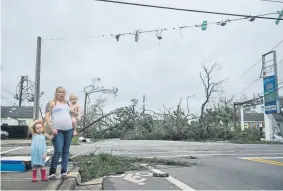  ?? Brendan Smialowski, AFP ?? A woman and her children wait near a destroyed gas station in Panama City, Fla. The hurricane left a path of destructio­n through the Florida Panhandle and entered Georgia as a Category 3 storm.