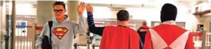  ??  ?? Superman impersonat­or Justin Harrison, center, high-fives a commuter wearing a sweatshirt with a Superman symbol printed on it as he and his roommate, Reginald Jackson, in a Red Power Ranger costume, head back home after working on Hollywood Boulevard.