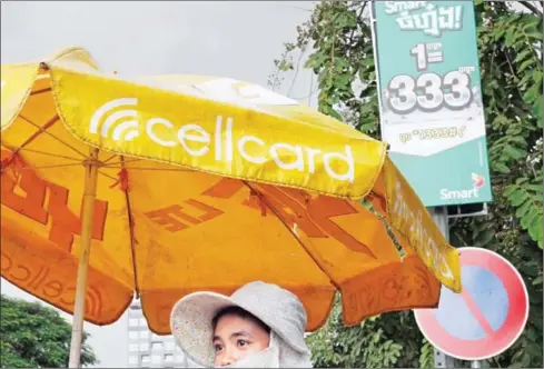  ?? PHA LINA ?? A woman stands under a Cellcard umbrella next to a Smart promotiona­l billboard yesterday in Phnom Penh.