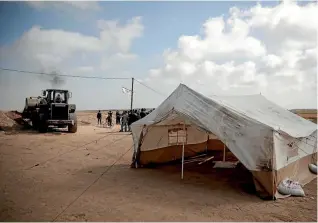  ?? PHOTO: AP ?? Palestinia­ns watch as a bulldozer raises protective sand berms around the tents at the Gaza Strip’s border with Israel.