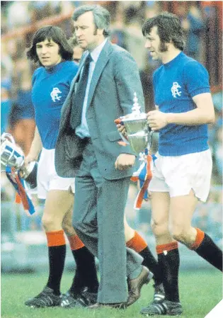  ??  ?? Gers boss Jock Wallace in 1975, as skipper John Greig carries the Scottish League First Division trophy and Johnny Hamilton the Reserve League version.