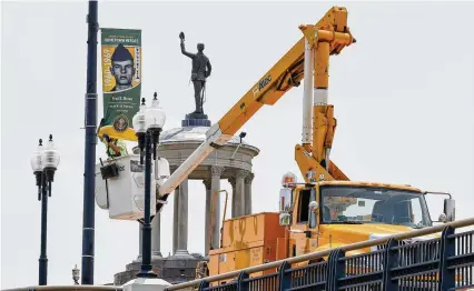  ?? NICK GRAHAM / STAFF ?? City crews install Hometown Heroes banners along the High Main Bridge with the Butler County Soldiers, Sailors and Pioneers Monument in the background Wednesday in Hamilton.